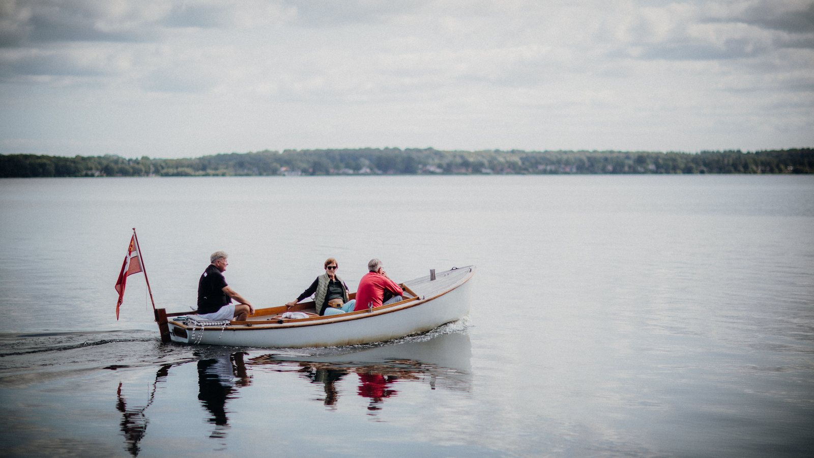 Kleines Holzboot mit drei Personen auf einem ruhigen See