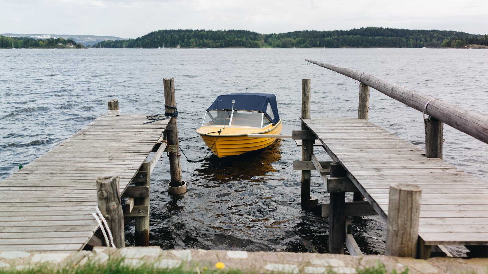 Kleines gelbes Motorboot zwischen zwei Holzstegen an einem See