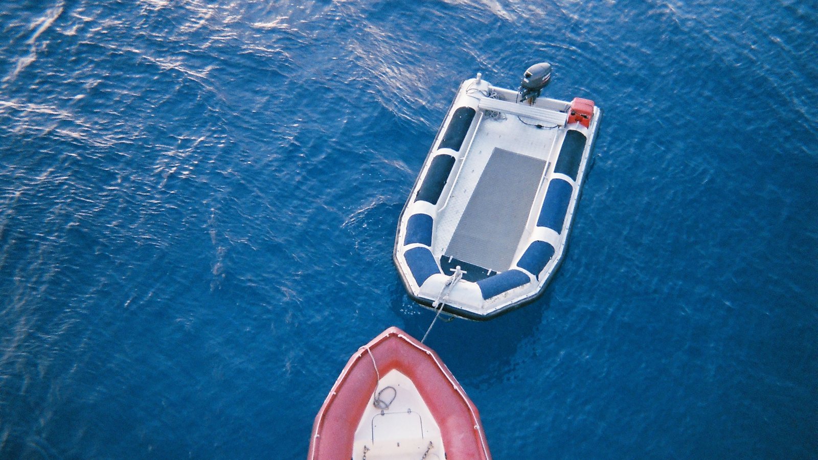 Kleines Schlauchboot mit Außenborder von oben, an einem roten Boot festgemacht